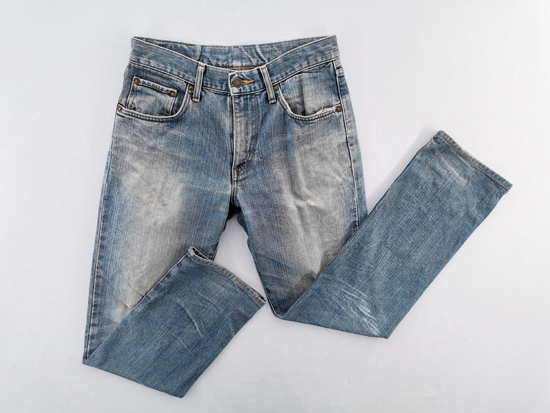 May include: Light blue denim jeans with a faded wash and classic five-pocket design. The jeans have a button and zipper closure, belt loops, and a straight leg cut. The fabric shows signs of wear, adding to the vintage aesthetic.