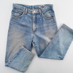 Op de afbeelding: Lichtblauwe denim jeans met een klassiek ontwerp met vijf zakken. De jeans hebben een knoop- en ritssluiting, riemlussen en het merklabel "Wrangler". De jeans zijn licht gewassen met vervaagde plekken.