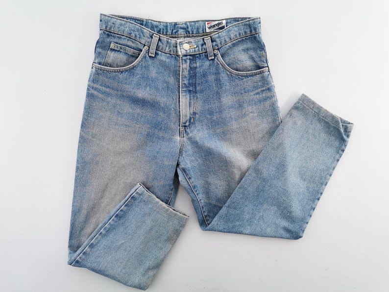 Op de afbeelding: Lichtblauwe denim jeans met een klassiek ontwerp met vijf zakken. De jeans hebben een knoop- en ritssluiting, riemlussen en het merklabel "Wrangler". De jeans zijn licht gewassen met vervaagde plekken.