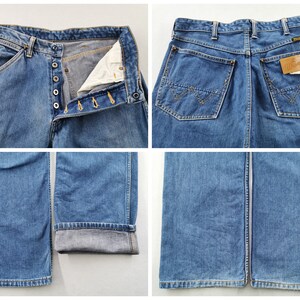 May include: Blue denim jeans with button fly closure and classic five-pocket design. The jeans feature a straight leg cut and a Wrangler brand label on the back pocket. The jeans are a medium wash and show signs of wear.