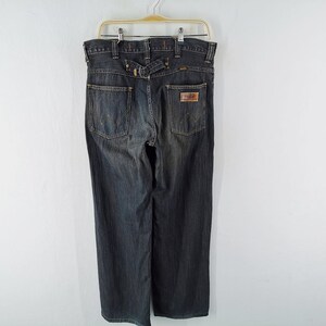 Peut inclure: Jean en denim d&eacute;lav&eacute; fonc&eacute; suspendu &agrave; un cintre. Le jean a une coupe droite, un patch en cuir sur la poche arri&egrave;re et un d&eacute;tail de passant de ceinture &agrave; la taille. Le jean est de style classique.