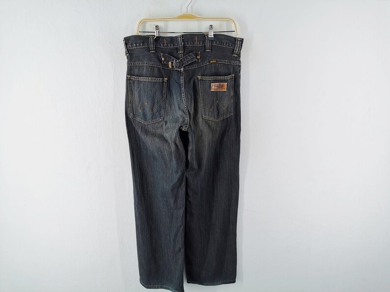 Peut inclure: Jean en denim d&eacute;lav&eacute; fonc&eacute; suspendu &agrave; un cintre. Le jean a une coupe droite, un patch en cuir sur la poche arri&egrave;re et un d&eacute;tail de passant de ceinture &agrave; la taille. Le jean est de style classique.