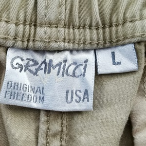 May include: Close-up of a tan fabric label with the brand name "GRAMICCI" and the words "ORIGINAL FREEDOM USA". The label also has a size "L" tag.