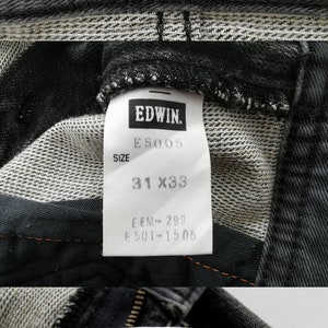 May include: Close-up of black denim jeans with visible tags. The tags display the brand "EDWIN", size 31x33, and care instructions. The jeans have a red tag with "Function Style" in orange lettering.