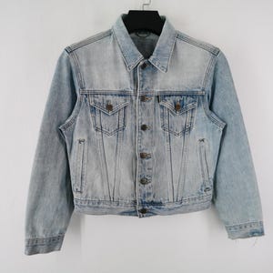 May include: Pale blue denim jacket with a traditional collar, button closure, and two breast pockets. The jacket has a faded appearance and a regular fit. A classic outerwear garment.