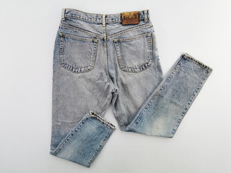 Op de afbeelding: Lichtblauwe acid wash jeans met een klassiek vijf-zakken ontwerp. De jeans hebben een rechte pijp en een leren patch met de merknaam "EDWIN" op de rug. De denim heeft een vervaagde, versleten uitstraling.