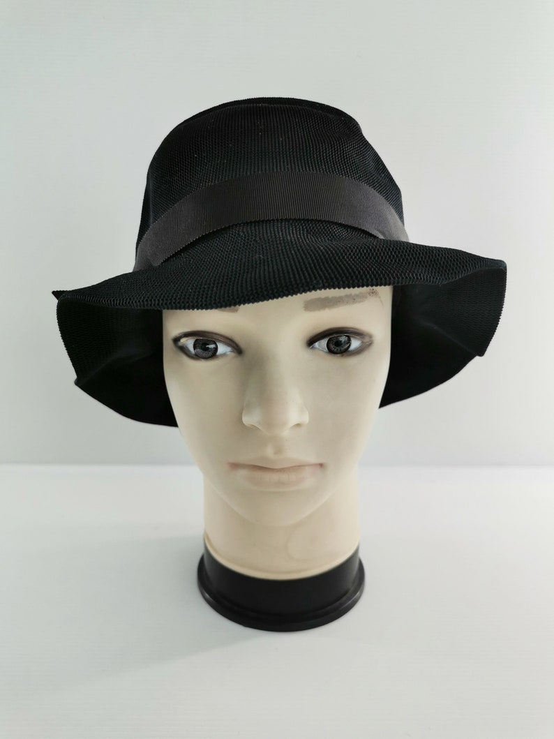 May include: A black hat with a wide brim and a black ribbon band. The hat is displayed on a mannequin head against a white background. The hat's material appears to be woven.
