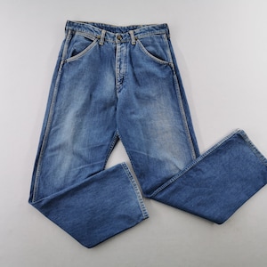 May include: Blue denim jeans with a button fly and classic five-pocket design. The jeans have a faded wash and a relaxed fit. The legs are slightly flared at the bottom. The jeans are laid flat on a white surface.