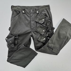 Puede incluir: Pantalones cargo de color gris oscuro con múltiples bolsillos y cierres de botón. Los pantalones tienen un diseño clásico con bragueta de botón y cremallera, trabillas para el cinturón y correas ajustables. Fabricados con tejido duradero.