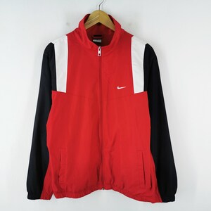 May include: Red, black, and white Nike track jacket with a full-length zipper. The jacket has a white Nike logo on the chest and white panels on the shoulders. The sleeves are black, and the body is red.