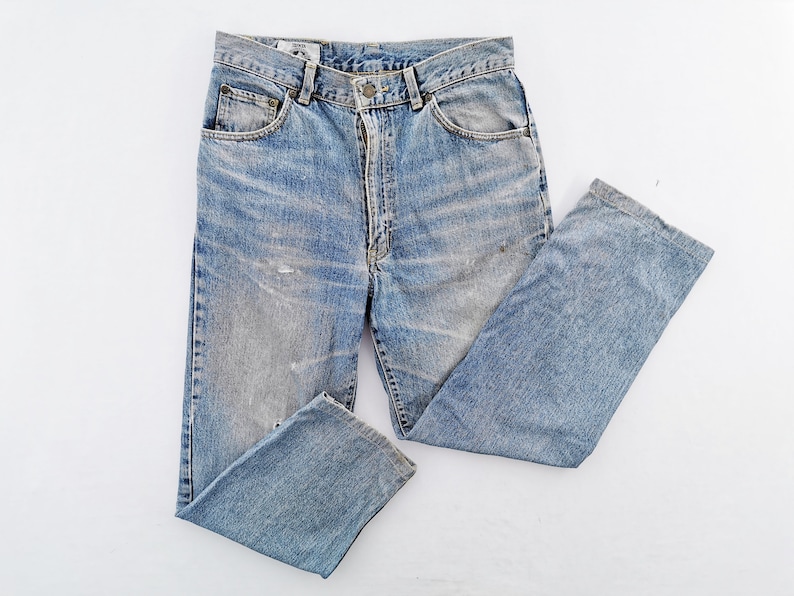 Puede incluir: Vaqueros de mezclilla azul claro con un lavado descolorido y detalles desgastados. Los vaqueros tienen un dise&ntilde;o cl&aacute;sico de cinco bolsillos, cierre de bot&oacute;n y cremallera, y corte recto. Estilo vintage.