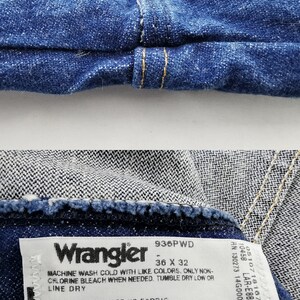 Puede incluir: Primer plano de unos vaqueros de mezclilla azules con una etiqueta Wrangler. La etiqueta indica una talla de 36 x 32. Los vaqueros est&aacute;n hechos de 100% algod&oacute;n y fabricados en M&eacute;xico.