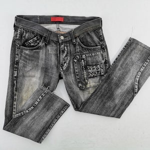 May include: Faded black denim jeans with a classic five-pocket design. Features include a button and zip closure, belt loops, and a small red tag on the waistband. The jeans have a distressed look with a unique pocket design.