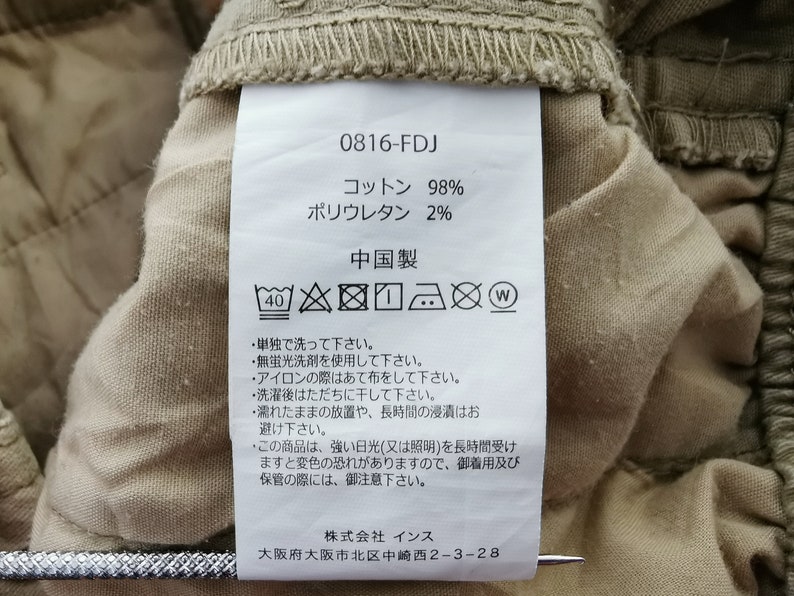 May include: Close-up of a clothing tag with the code 0816-FDJ. The tag indicates the fabric is 98% cotton and 2% polyurethane. Washing instructions are also printed on the tag.