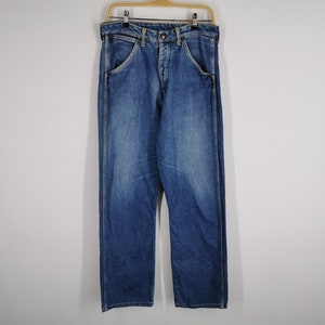 May include: Blue denim jeans hanging on a wooden hanger. The jeans have a classic five-pocket design, a button and zipper closure, and a straight leg cut. The denim has a faded wash, with lighter areas on the thighs and knees.