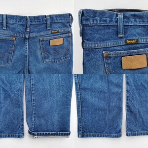 May include: Blue denim Wrangler jeans with a classic five-pocket design. Features a brown leather patch and the Wrangler logo. The jeans have a straight leg and are cuffed at the bottom.