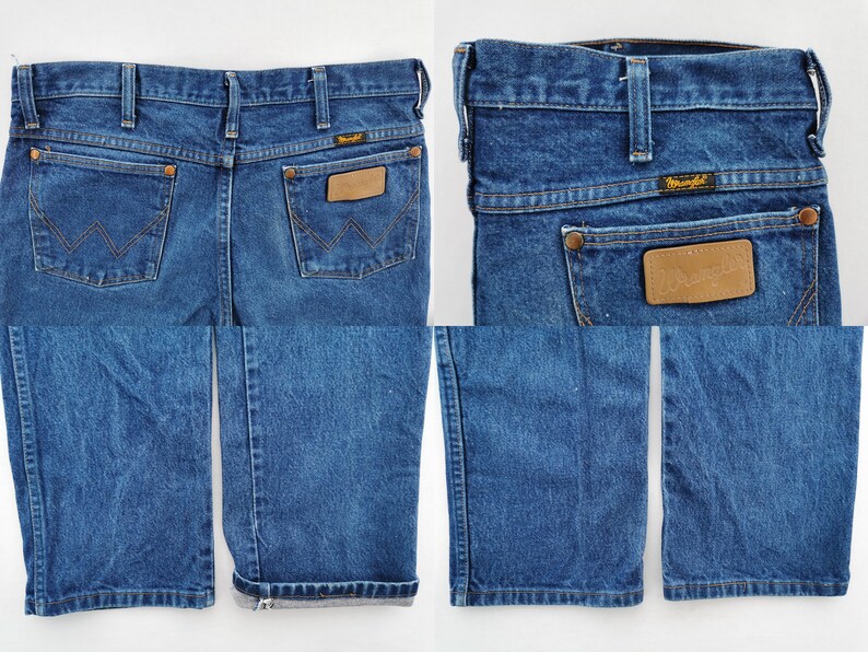 May include: Blue denim Wrangler jeans with a classic five-pocket design. Features a brown leather patch and the Wrangler logo. The jeans have a straight leg and are cuffed at the bottom.