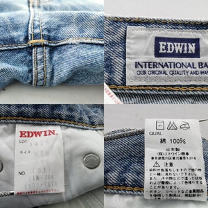 Puede incluir: Primer plano de unos vaqueros de mezclilla azul claro con costuras y etiquetas visibles. Las etiquetas muestran la marca "EDWIN" y detalles como "INTERNATIONAL BASIC". Los vaqueros tienen un dise&ntilde;o cl&aacute;sico.