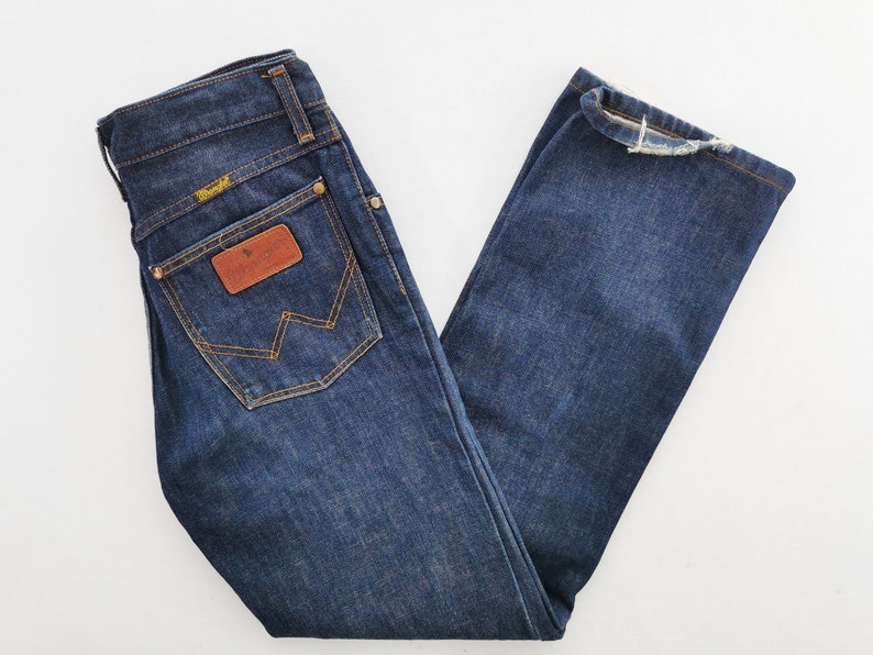 Op de afbeelding: Donkerblauwe denim jeans met een klassiek vijf-zakken ontwerp. Voorzien van een bruine leren patch en het Wrangler-logo op de achterzak. De jeans heeft een rechte pijp en is netjes opgevouwen.