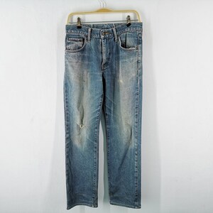 May include: Blue denim jeans with a distressed look, featuring a faded wash and a ripped knee. The jeans are hanging on a gold-colored hanger against a white background. The jeans have classic five-pocket styling.