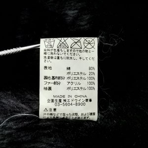 Puede incluir: Primer plano de una tela negra con una etiqueta adjunta. La etiqueta contiene texto japon&eacute;s y s&iacute;mbolos de cuidado, junto con detalles de la composici&oacute;n de la tela: 80% algod&oacute;n, 20% poli&eacute;ster y 100% acr&iacute;lico para la parte de la piel. Hecho en China.