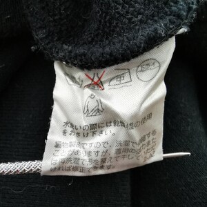 以下が含まれることがあります： 黒い衣服のクローズアップ。白いケアラベルが付いています。ラベルには、アイロン禁止マークやタンブル乾燥禁止マークなど、いくつかのケアシンボルが表示されています。日本語のテキストも表示されています。