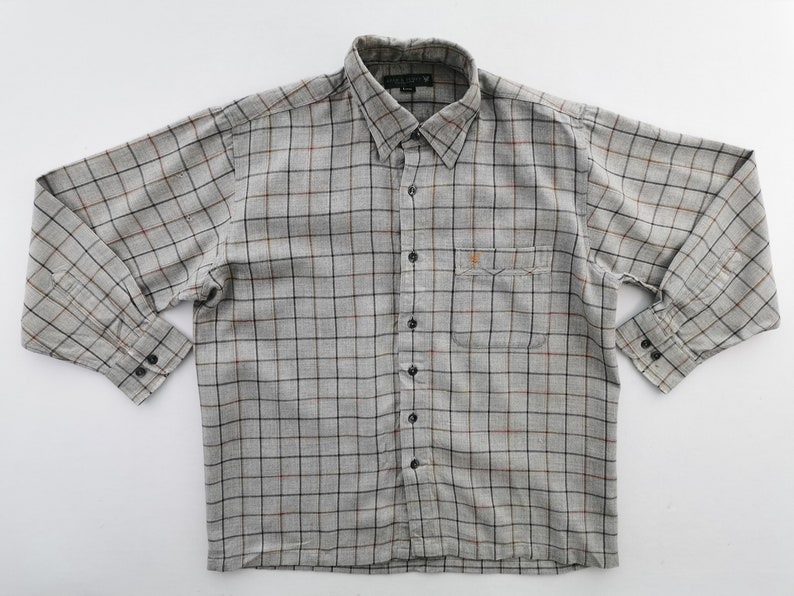 以下が含まれることがあります： 長袖のグレーのチェック柄シャツ。ボタンダウンカラー、胸ポケット、黒いボタンが付いています。チェック柄は黒、赤、茶色の線で構成されています。シャツは白い背景に平らに置かれています。