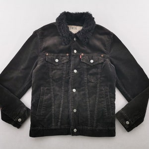 Puede incluir: Chaqueta de pana negra con cuello de piel sint&eacute;tica. La chaqueta tiene cierre de botones, dos bolsillos en el pecho y dos bolsillos laterales. La marca "EDWIN" es visible en el cuello.