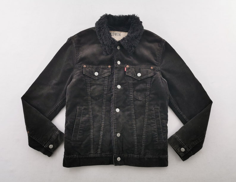 Puede incluir: Chaqueta de pana negra con cuello de piel sint&eacute;tica. La chaqueta tiene cierre de botones, dos bolsillos en el pecho y dos bolsillos laterales. La marca "EDWIN" es visible en el cuello.