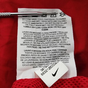 May include: Close-up of a red garment with a white care label. The label includes washing instructions in multiple languages, along with the Nike logo and product code.