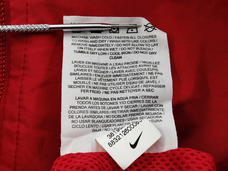 May include: Close-up of a red garment with a white care label. The label includes washing instructions in multiple languages, along with the Nike logo and product code.