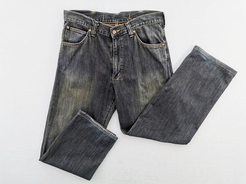 Peut inclure: Un jean en denim noir d&eacute;lav&eacute; avec une conception classique &agrave; cinq poches. Le jean a une fermeture &agrave; bouton et &agrave; glissi&egrave;re, des passants de ceinture et un aspect l&eacute;g&egrave;rement us&eacute;. Le jean est pos&eacute; &agrave; plat sur une surface blanche.