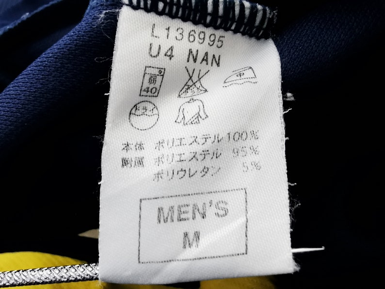 May include: A white clothing label with black text and symbols. The label shows the text "L136995", "U4 NAN", and "MEN'S M". It also includes washing instructions and fabric composition details.