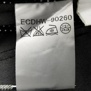 May include: A white fabric tag with the text "ECDHW-90260" and several laundry symbols. The tag is attached to a dark gray fabric with a subtle striped pattern. The background includes a white polka dot pattern.