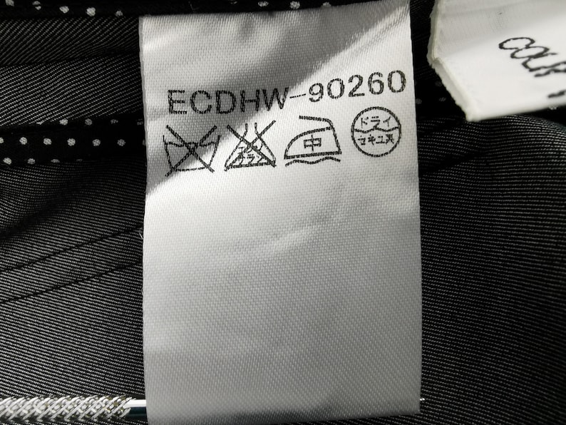 May include: A white fabric tag with the text "ECDHW-90260" and several laundry symbols. The tag is attached to a dark gray fabric with a subtle striped pattern. The background includes a white polka dot pattern.