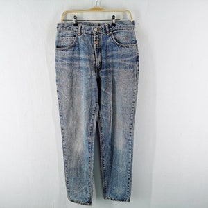 Op de afbeelding: Acid wash denim jeans met een knoopsluiting en een klassiek ontwerp met vijf zakken. De jeans hangen aan een gouden hanger tegen een witte achtergrond. De jeans hebben een vervaagde, versleten look.