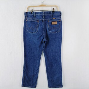 May include: Dark blue denim jeans hanging on a hanger. The jeans have a classic five-pocket design, a straight leg, and a brown leather patch with the brand name. The back pockets feature a distinctive stitched design.