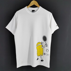 May include: White t-shirt with a cartoon tennis player graphic. The graphic features a yellow character with a headband holding a tennis racket, with a tennis ball and Japanese text. Nike logo on the sleeve.