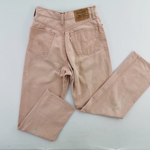 May include: A pair of light pink denim jeans with a classic five-pocket design. The jeans feature a high waist and a straight leg cut. The Levi's brand label is visible on the back pocket. The jeans are laid flat on a white surface.