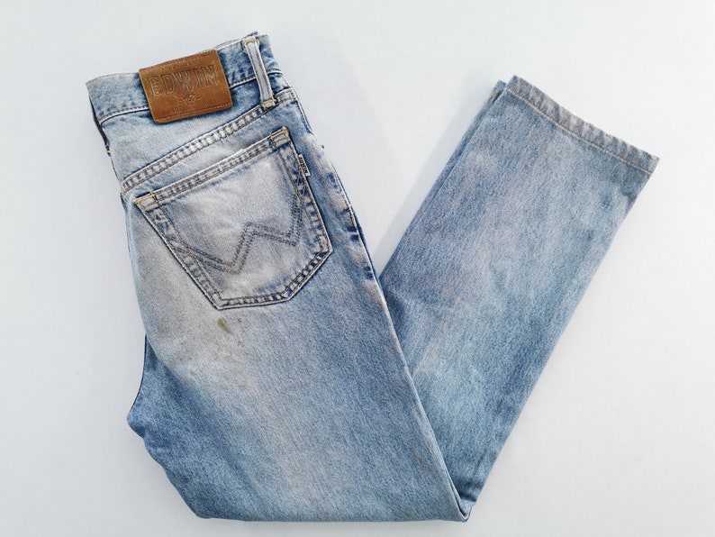 Puede incluir: Vaqueros de mezclilla azul claro con un lavado descolorido y un parche de cuero marr&oacute;n. Los vaqueros presentan un dise&ntilde;o cl&aacute;sico de cinco bolsillos y un corte de pierna recta. El bolsillo trasero tiene un dise&ntilde;o cosido distintivo.