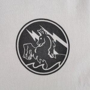 Puede incluir: Camiseta blanca con un dise&ntilde;o circular negro. El dise&ntilde;o muestra una criatura parecida a un caballo con rayos y olas. El dise&ntilde;o est&aacute; centrado, ofreciendo un contraste llamativo.