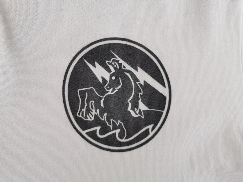 Puede incluir: Camiseta blanca con un dise&ntilde;o circular negro. El dise&ntilde;o muestra una criatura parecida a un caballo con rayos y olas. El dise&ntilde;o est&aacute; centrado, ofreciendo un contraste llamativo.