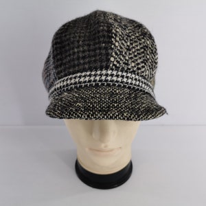 Pode incluir: Um boné estilo newsboy com um design de retalhos em tecido de mistura de lã preta, branca e cinzenta. O chapéu apresenta uma mistura de padrões de pé-de-galinha e tweed, com uma faixa horizontal de acabamento sobre a aba rígida.