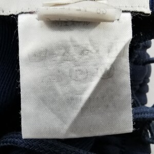 Puede incluir: Primer plano de una etiqueta de tela blanca con texto descolorido, adherida a una prenda azul marino. La etiqueta es rectangular con un borde doblado. Se ve un cord&oacute;n azul marino.