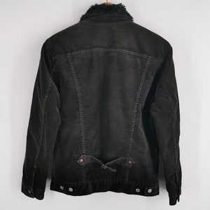Puede incluir: Chaqueta de pana gris oscuro con cuello de piel sint&eacute;tica negra. La chaqueta tiene cierre de botones, dos bolsillos delanteros y un detalle de cintur&oacute;n en la espalda. La chaqueta se muestra sobre un fondo blanco.