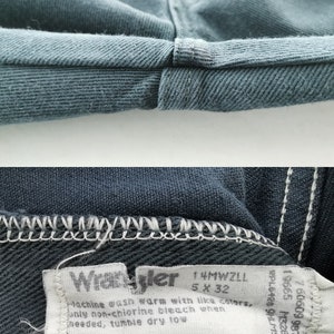 K&ouml;nnte beinhalten: Nahaufnahme einer blauen Jeans, die den gefalteten Saum und ein Etikett zeigt. Das Etikett tr&auml;gt die Aufschrift "Wrangler" und enth&auml;lt Gr&ouml;&szlig;enangaben: 5 x 32. Die Jeans besteht aus 100 % Baumwolle und ist maschinenwaschbar.