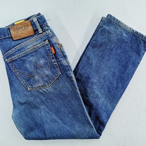 May include: Blue denim jeans with a classic five-pocket design. Features a brown leather patch with "EDWIN US CLASSIC" branding and a red logo tag. The jeans have a straight leg cut.