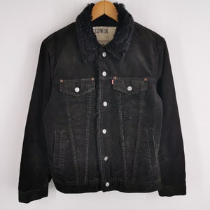 Puede incluir: Chaqueta de pana negra con cuello de piel sint&eacute;tica. La chaqueta tiene dos bolsillos en el pecho y dos bolsillos laterales, con botones plateados y una etiqueta roja. La chaqueta es de la marca Edwin.