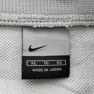 Puede incluir: Primer plano de una tela gris con una etiqueta negra de Nike. La etiqueta presenta el logotipo de Nike, indicadores de talla XL, TG, EG y el texto "MADE IN JAPAN". La tela tiene un patr&oacute;n texturizado en forma de rejilla.