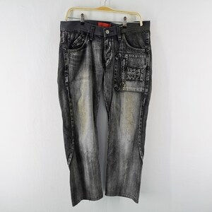 May include: Faded black denim jeans with unique pocket details. Features a patch pocket on the right leg and standard pockets. The jeans are hanging on a wooden hanger against a white background.